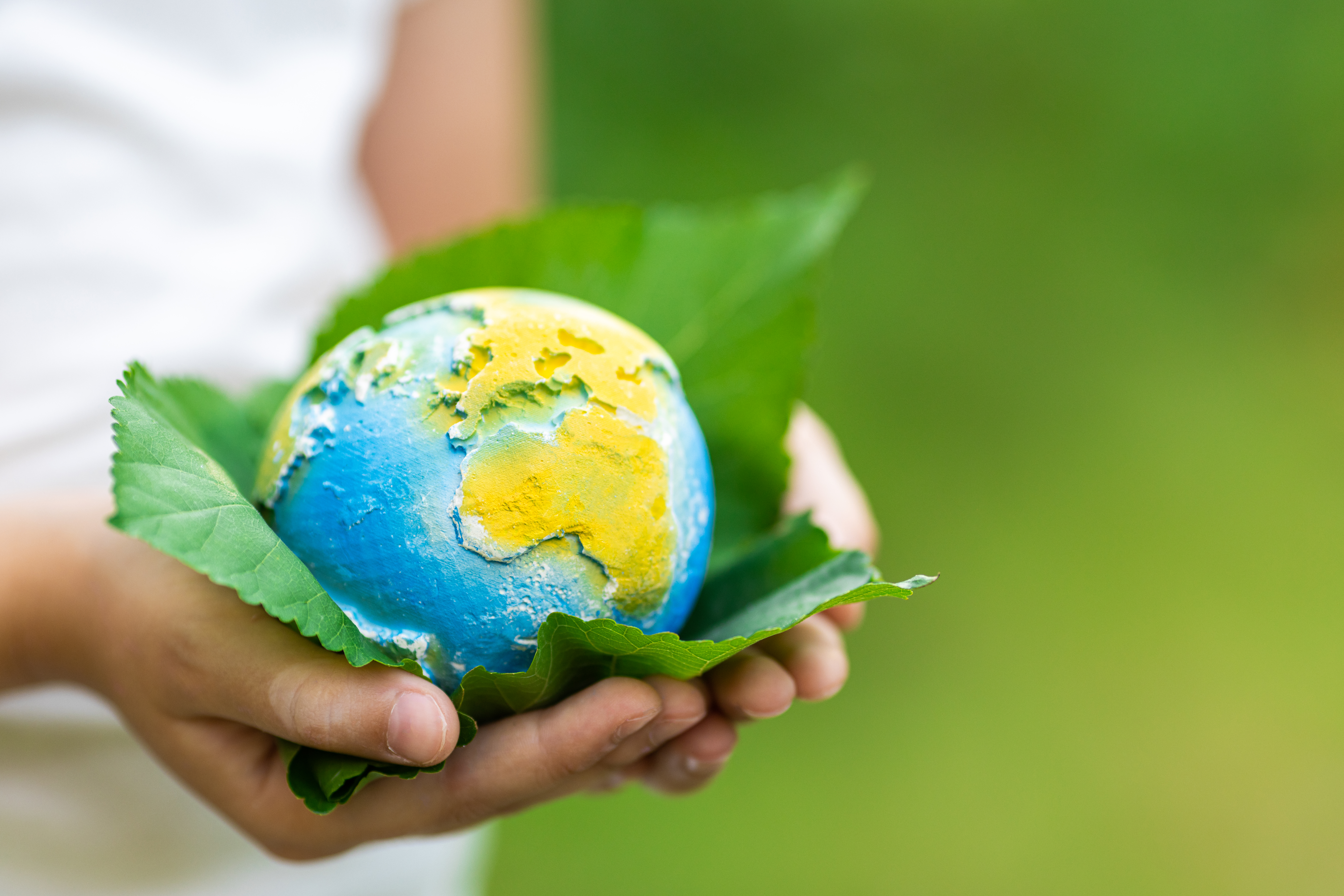Kid holding small planet in hands against spring or summer green background. Ecology, environment and Earth day concept.